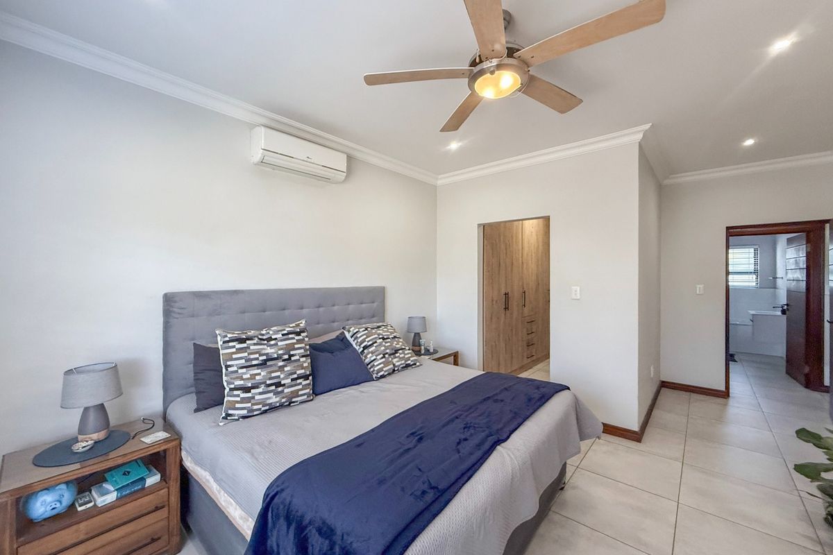 Spacious bedroom featuring tiled flooring, built-in cupboards, a ceiling fan, and a wall-mounted air conditioning unit, with an adjoining en-suite bathroom.