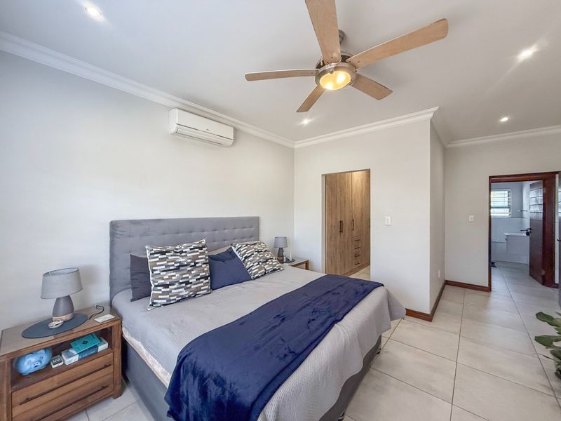 Spacious bedroom featuring tiled flooring, built-in cupboards, a ceiling fan, and a wall-mounted air conditioning unit, with an adjoining en-suite bathroom.