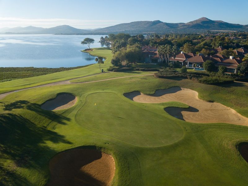 Aerial view of a pristine golf course green featuring sand bunkers, overlooking a scenic lake and surrounding residential estate.