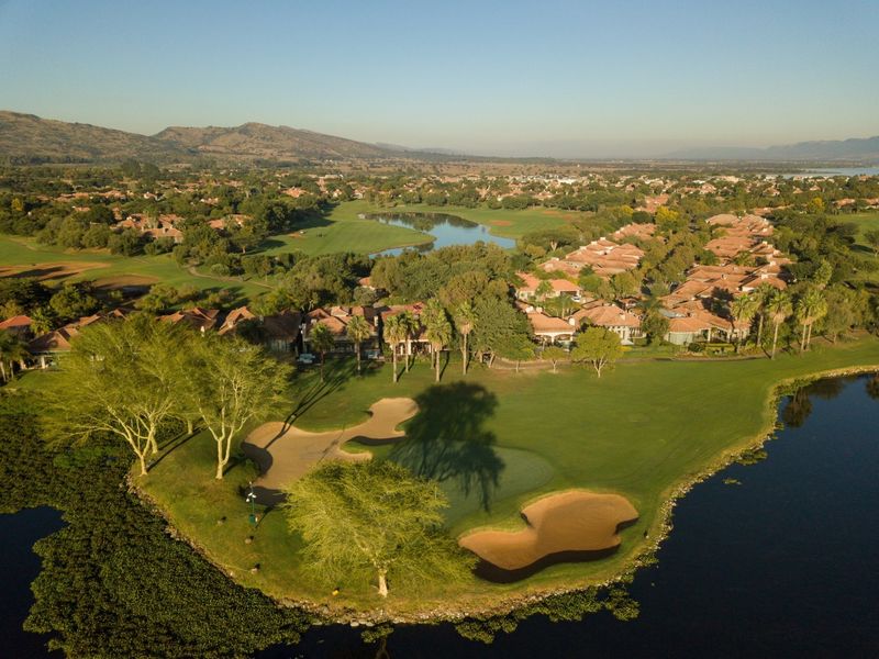 Aerial view of a residential estate featuring a golf course, water hazards, and manicured green spaces in a scenic landscape setting.