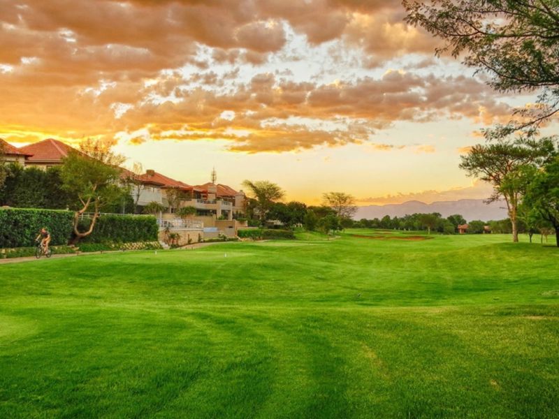 A scenic view of a well-maintained golf course landscape with mature trees and a paved pathway at sunset.