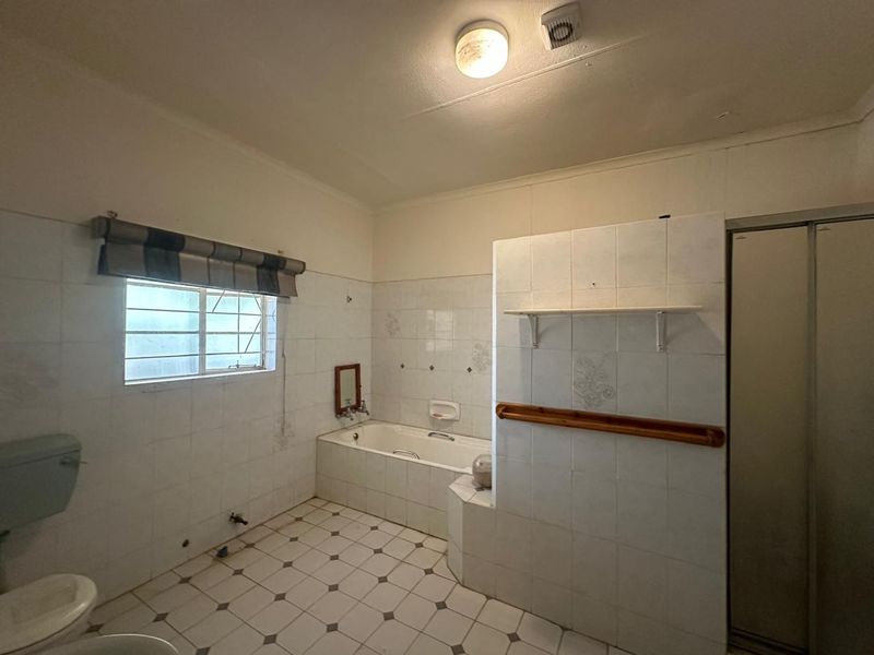 A spacious, dated bathroom featuring a built-in bathtub, separate shower enclosure, and full-height wall tiling, offering significant potential for a modern renovation.