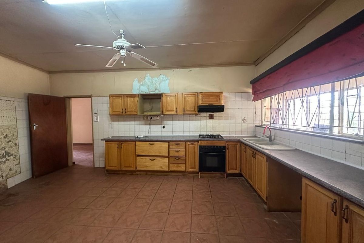 Spacious kitchen featuring wooden cabinetry, built-in oven, gas hob, and double basin sink, requiring cosmetic updates to address wall damage and dated finishes.