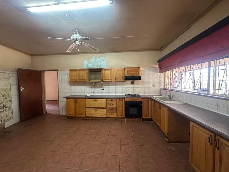 Spacious kitchen featuring wooden cabinetry, built-in oven, gas hob, and double basin sink, requiring cosmetic updates to address wall damage and dated finishes.