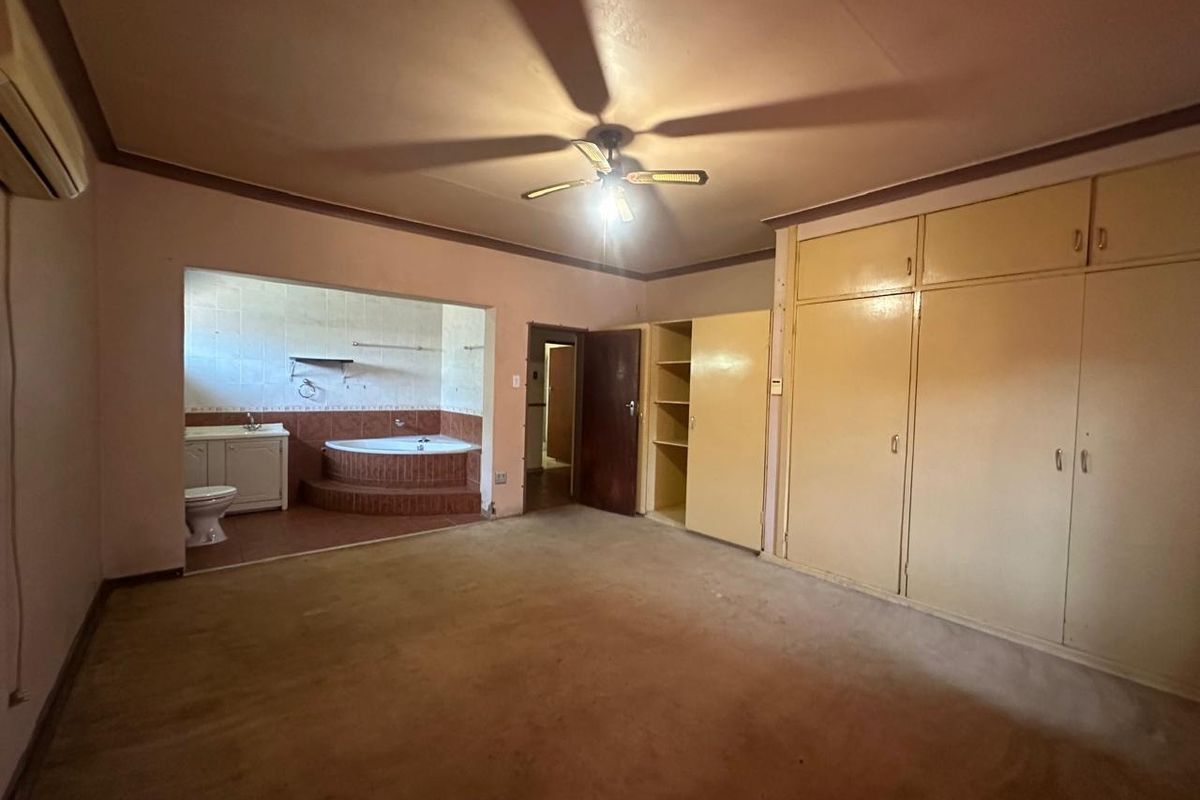 Spacious bedroom featuring built-in cupboards, an air conditioning unit, and an open-plan en-suite bathroom with a corner bathtub and vanity.