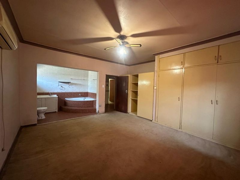Spacious bedroom featuring built-in cupboards, an air conditioning unit, and an open-plan en-suite bathroom with a corner bathtub and vanity.