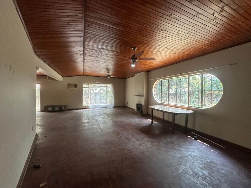 Spacious living area featuring a distinctive timber-clad vaulted ceiling, built-in fireplace, and large windows with security bars, offering a blank canvas for renovation.