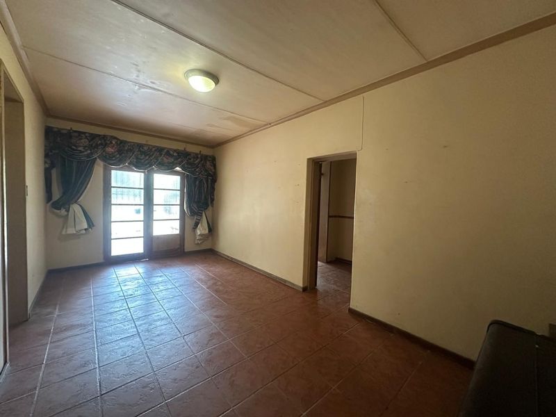 An empty living room featuring tiled flooring, a sliding glass door, and a ceiling light fixture, showing signs of wear and requiring cosmetic updates.