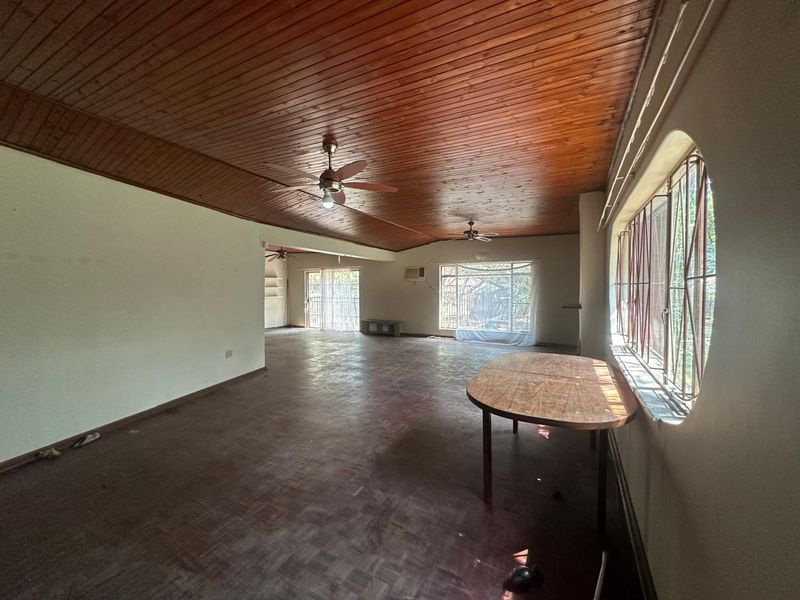 Spacious open-plan living area featuring a classic wooden ceiling, parquet flooring, and large windows with security bars.