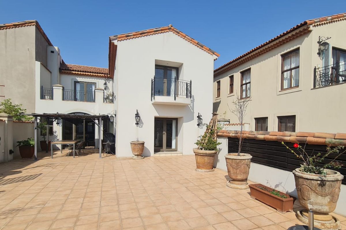 Spacious rear patio area featuring terracotta tiling, a pergola, and a two-story building facade with a balcony and classic architectural details.