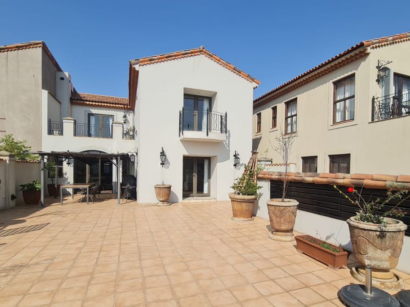 Spacious rear patio area featuring terracotta tiling, a pergola, and a two-story building facade with a balcony and classic architectural details.