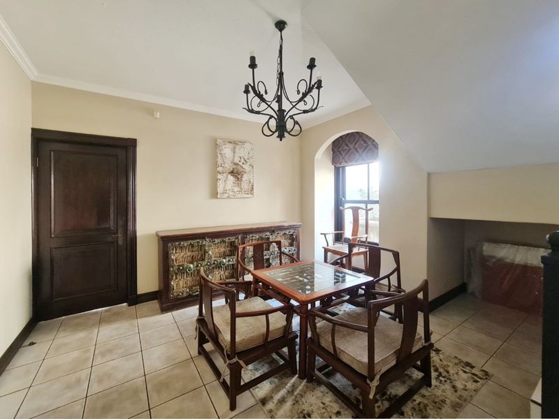 A dining area featuring tiled flooring, a wrought iron chandelier, and an arched window, providing a classic and well-maintained space for meals.