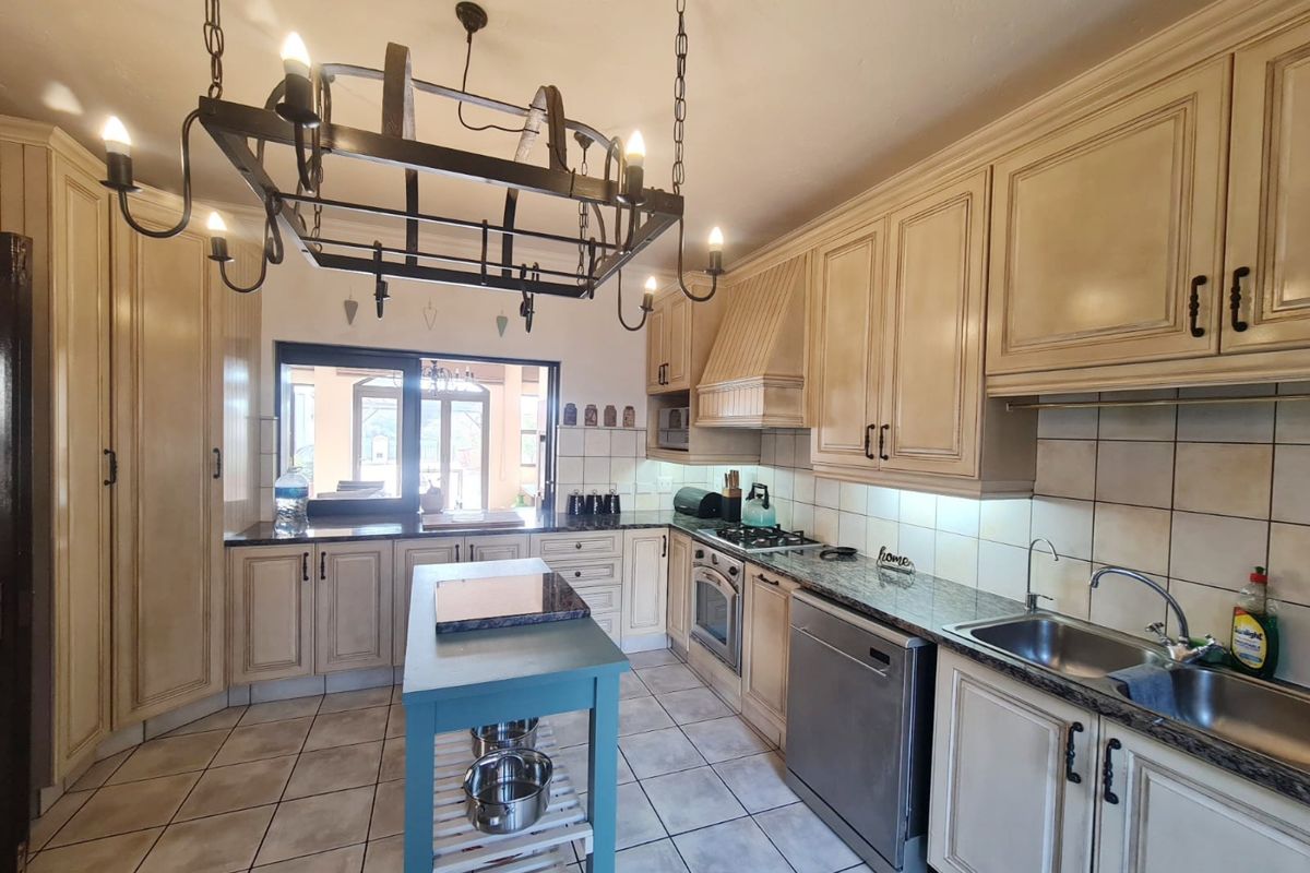 A spacious kitchen featuring classic cream cabinetry, granite countertops, integrated appliances, and a distinctive wrought iron chandelier, offering a functional and traditional cooking space.