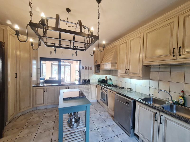 A spacious kitchen featuring classic cream cabinetry, granite countertops, integrated appliances, and a distinctive wrought iron chandelier, offering a functional and traditional cooking space.