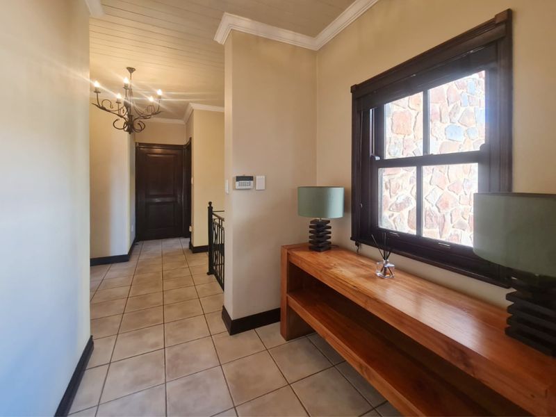 A well-maintained hallway featuring tiled floors, timber window frames, and a wrought iron balustrade leading to an adjacent area.