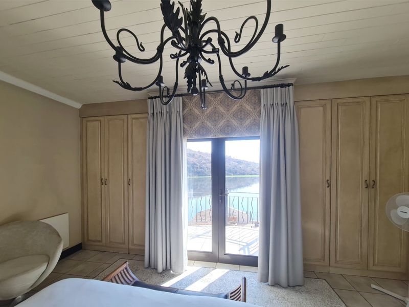 Spacious bedroom featuring extensive built-in cabinetry, a decorative chandelier, and double doors opening onto a balcony with scenic water views.