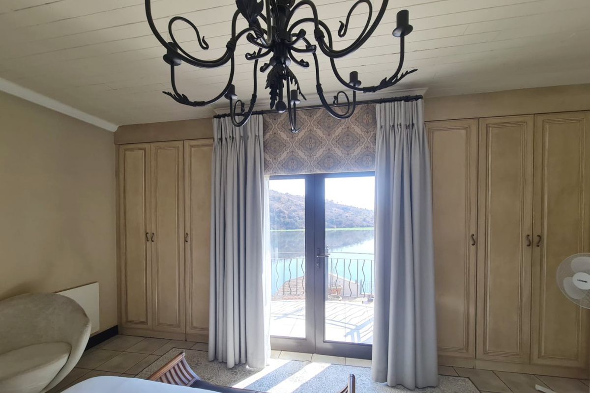 Spacious bedroom featuring extensive built-in cabinetry, a decorative chandelier, and double doors opening onto a balcony with scenic water views.