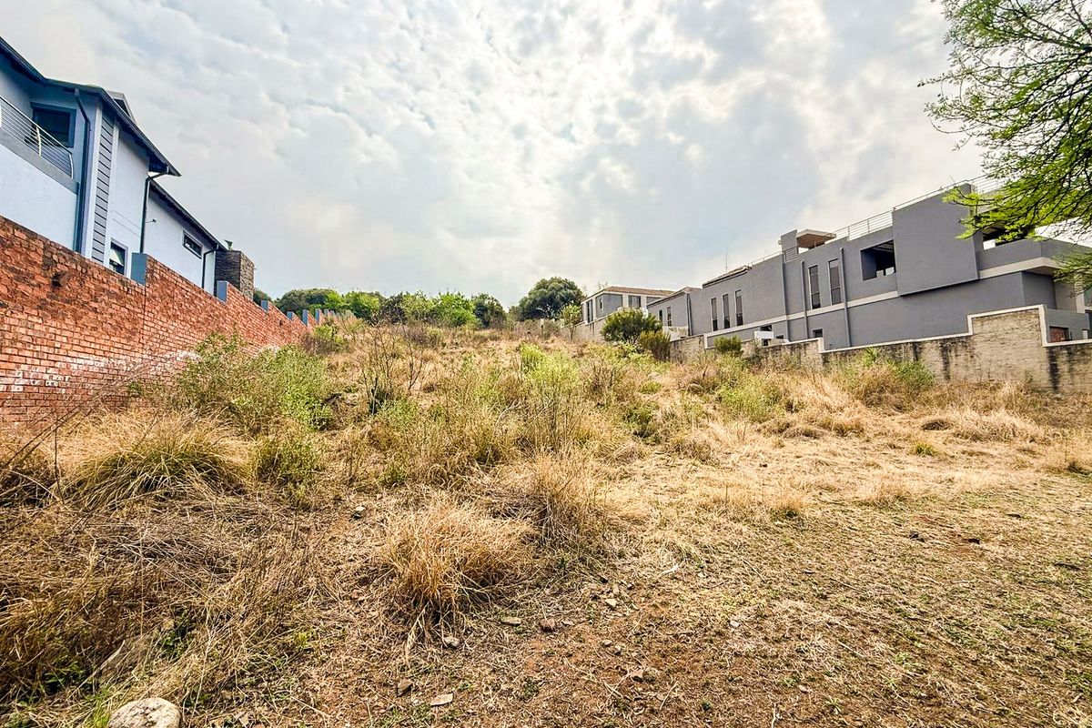A vacant residential plot featuring a sloped landscape, enclosed by brick boundary walls and situated between existing modern residential developments.