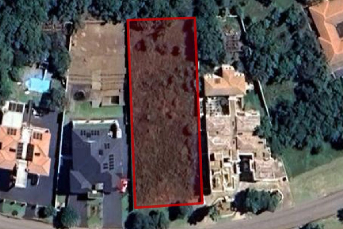An aerial view of a vacant residential land plot situated between existing developed properties in a suburban neighborhood.