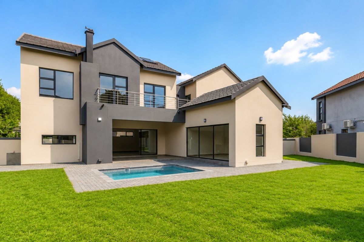 Rear view of a modern two-story house featuring a swimming pool, paved patio area, balcony, and a well-maintained garden.