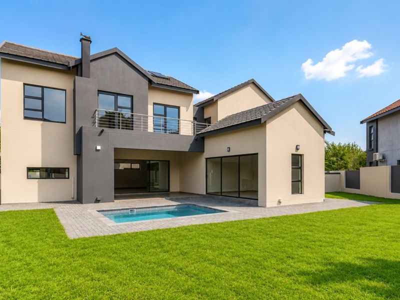 Rear view of a modern two-story house featuring a swimming pool, paved patio area, balcony, and a well-maintained garden.