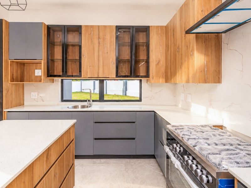 Modern kitchen featuring two-tone wood and grey cabinetry, quartz countertops, a central island, and a high-end gas stove with an integrated extractor fan.