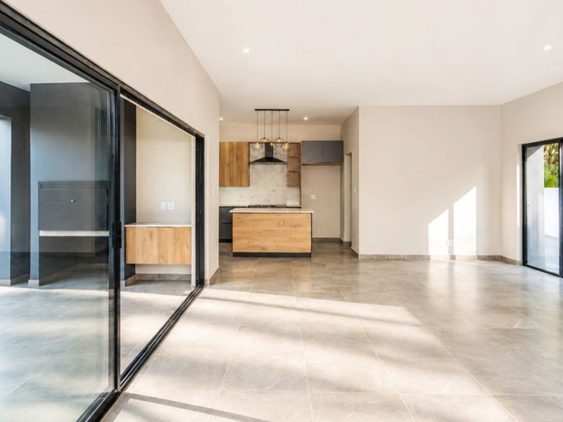 Spacious open-plan living area featuring a modern kitchen with wood-finish cabinetry, large sliding glass doors, and neutral tiled flooring throughout.