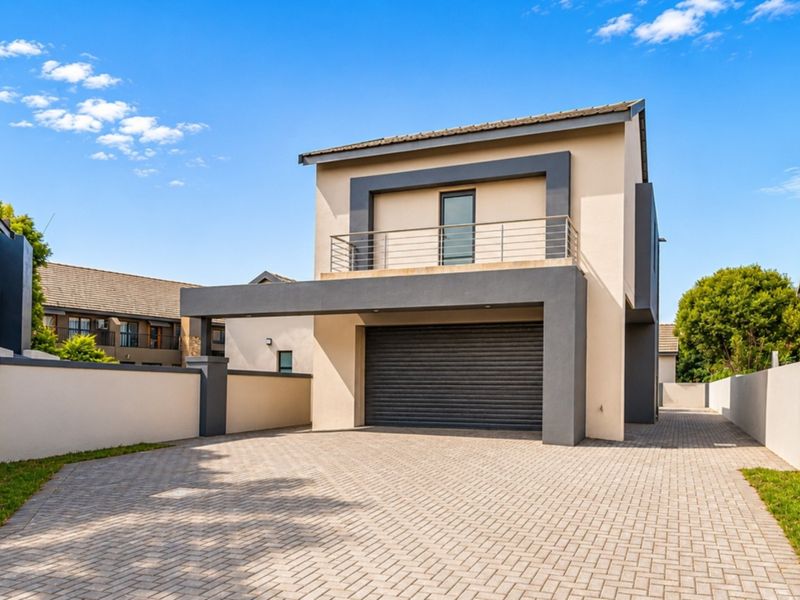 Modern double-story residential property featuring a paved driveway, secure roller garage door, and an upper-level balcony with contemporary architectural finishes.