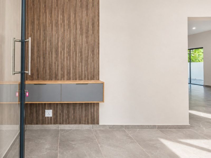 Modern hallway featuring timber slat wall paneling, floating cabinetry, and neutral porcelain floor tiles, leading into an open-plan living area.