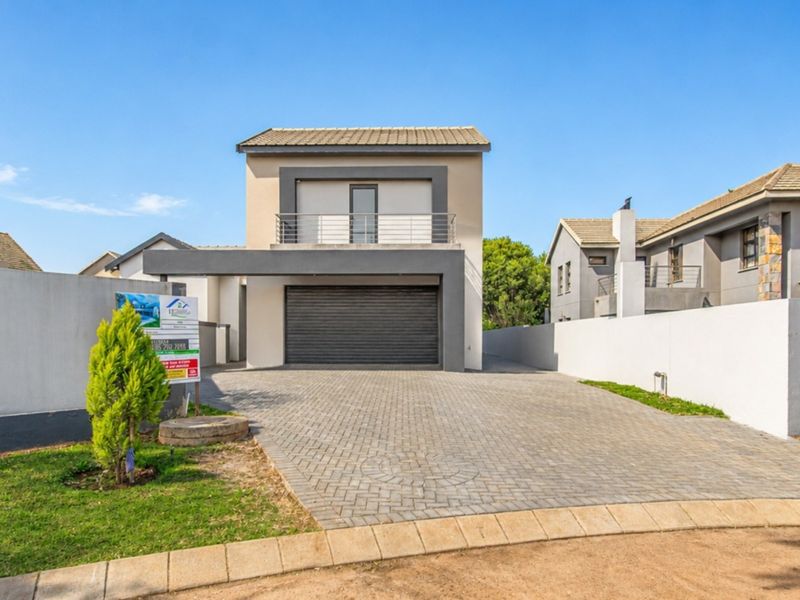 Modern double-story residential property featuring a paved driveway, secure roller garage door, and an upper-level balcony with metal railing.