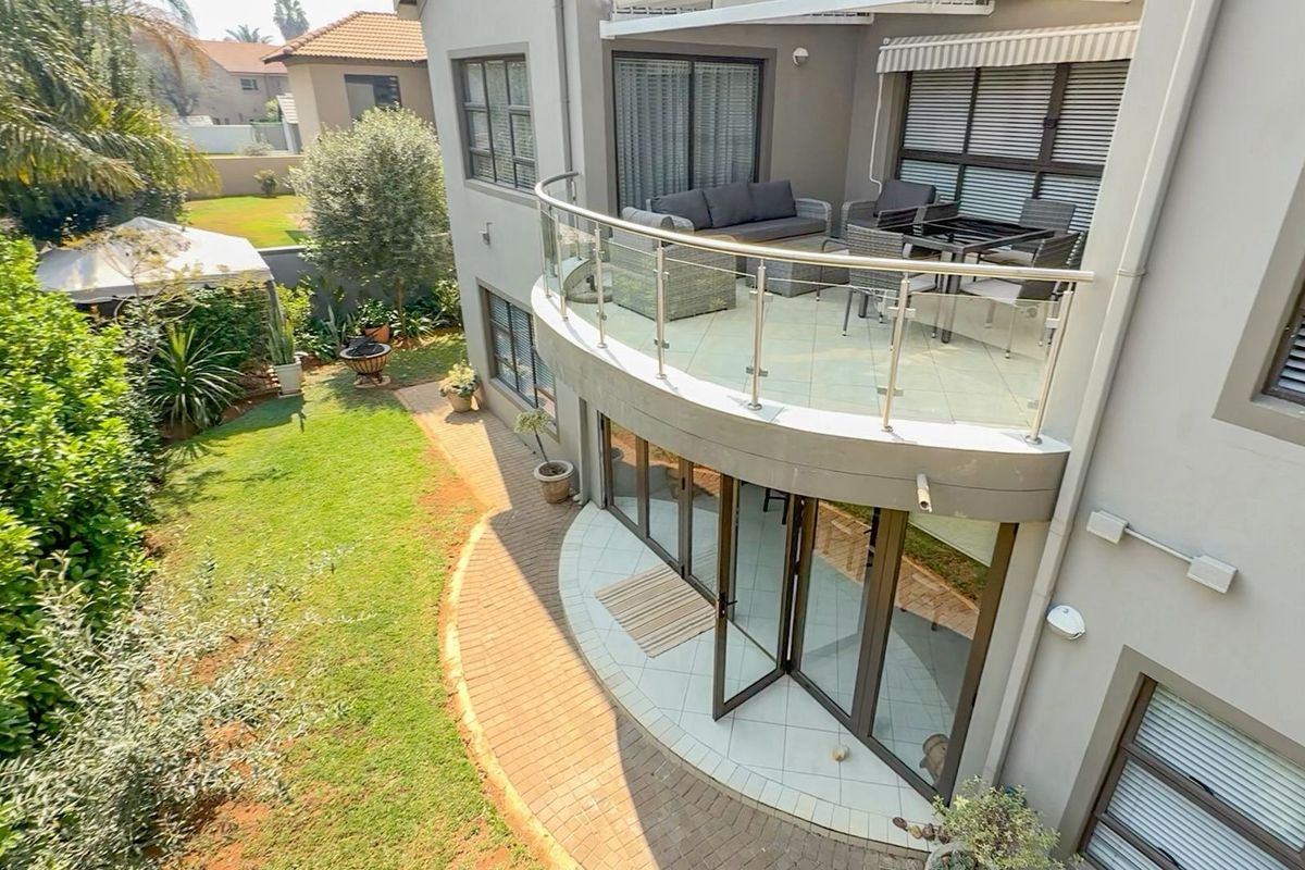 Elevated view of the rear exterior featuring a curved balcony with glass balustrades, tiled patio area, and bi-fold doors leading to a landscaped garden.