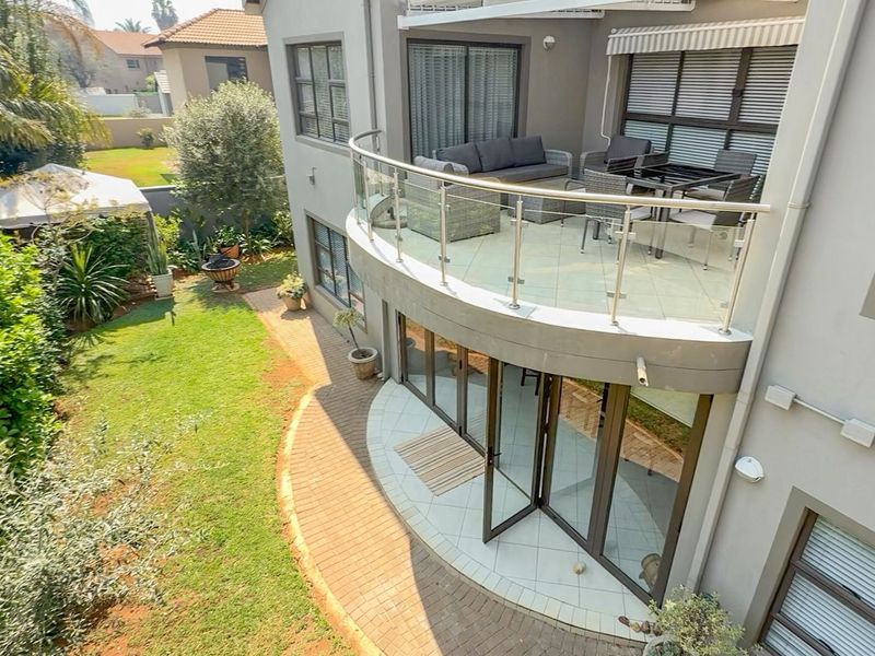 Elevated view of the rear exterior featuring a curved balcony with glass balustrades, tiled patio area, and bi-fold doors leading to a landscaped garden.