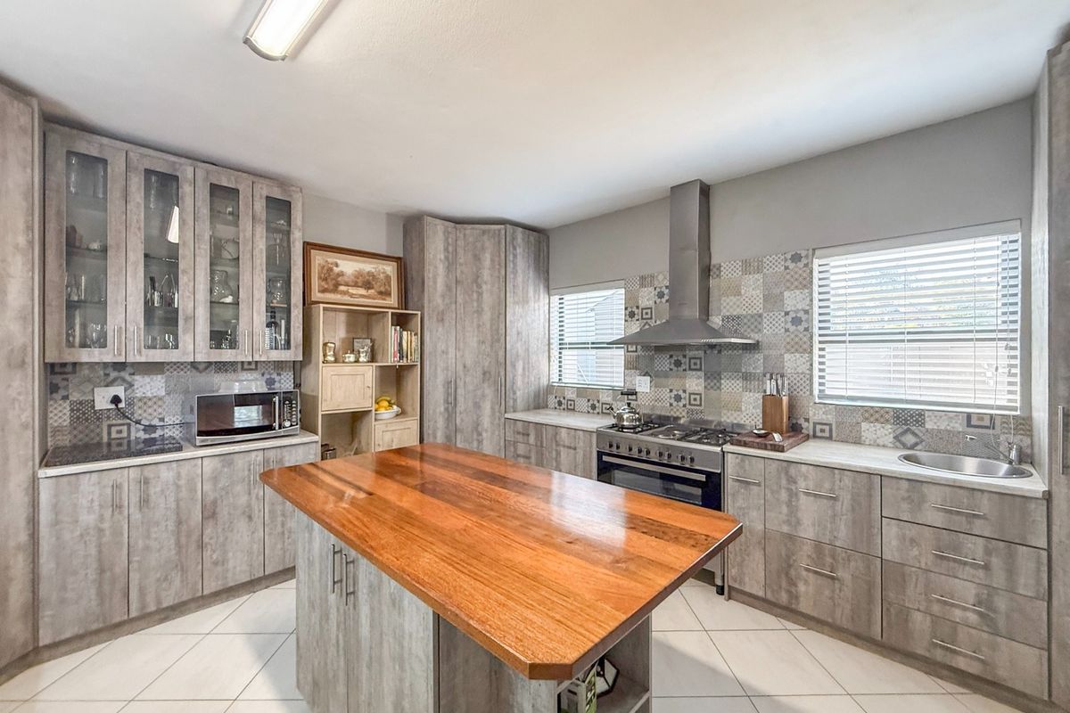 Modern kitchen featuring grey wood-look cabinetry, a central island with a wooden countertop, gas stove, extractor fan, and decorative tiled backsplash.