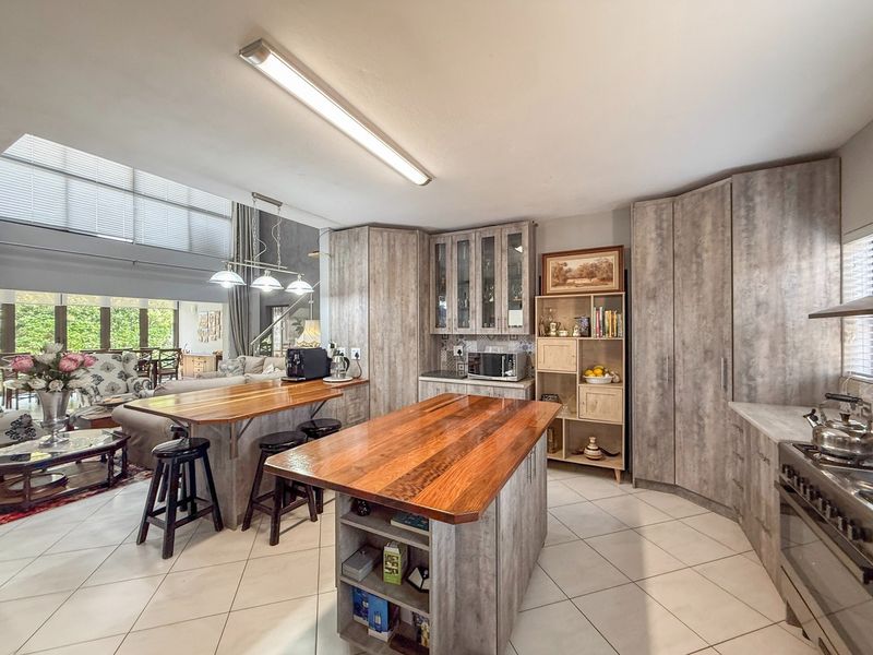 Spacious open-plan kitchen featuring a wooden breakfast bar, central island, modern cabinetry, and tiled flooring, seamlessly flowing into the adjacent living area.