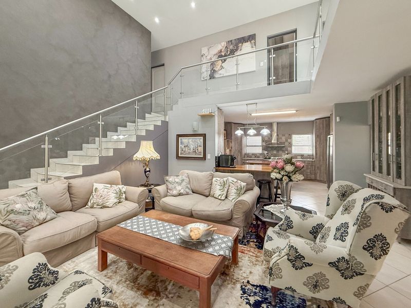 Spacious open-plan living area featuring a modern staircase with glass balustrades, tiled flooring, and a well-appointed kitchen with built-in cabinetry and island.