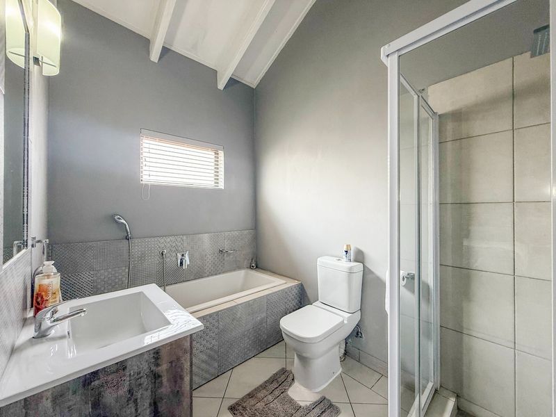 Modern bathroom featuring a built-in bathtub, separate shower enclosure, vanity cabinet, and toilet, complemented by tiled finishes and a vaulted ceiling.