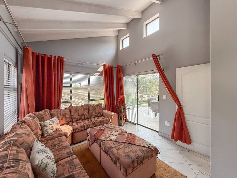Spacious living room featuring high vaulted ceilings with exposed beams, tiled flooring, and large sliding glass doors providing access to an outdoor patio area.