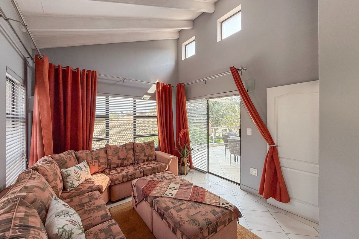 Spacious living room featuring high vaulted ceilings with exposed beams, tiled flooring, and large sliding glass doors providing access to an outdoor patio area.