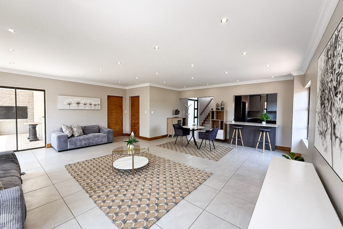 Spacious open-plan living and dining area featuring neutral tiled flooring, recessed downlighting, and a breakfast bar connecting to the kitchen.