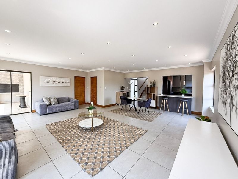 Spacious open-plan living and dining area featuring neutral tiled flooring, recessed downlighting, and a breakfast bar connecting to the kitchen.