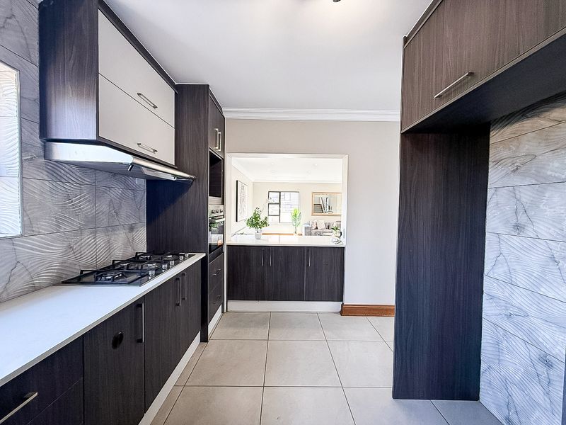 Modern kitchen featuring dark wood cabinetry, stone countertops, a gas hob with extractor, and stylish textured wall tiling, leading into an open-plan living area.