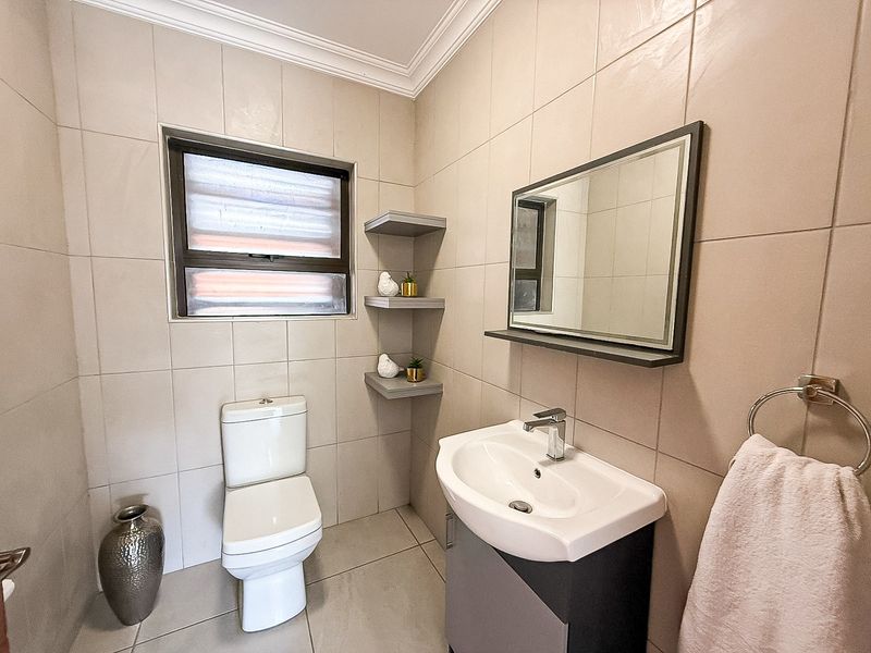 A well-maintained bathroom featuring a modern vanity with basin, wall-mounted mirror, toilet, and neutral floor-to-ceiling wall tiles.