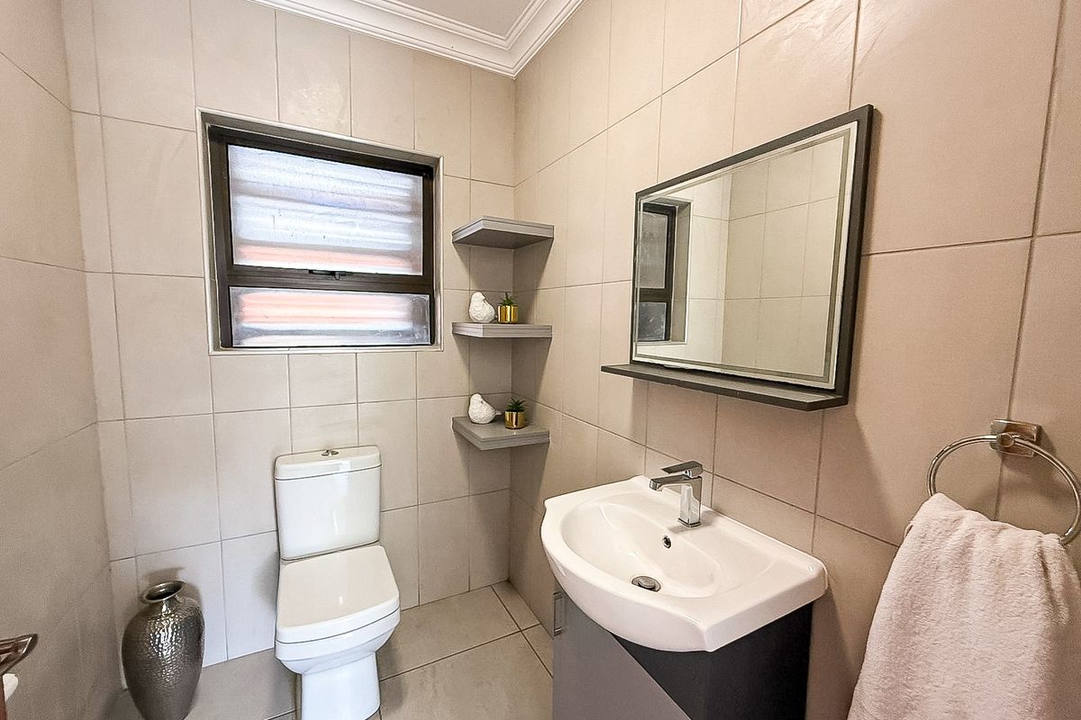 A well-maintained bathroom featuring a modern vanity with basin, wall-mounted mirror, toilet, and neutral floor-to-ceiling wall tiles.
