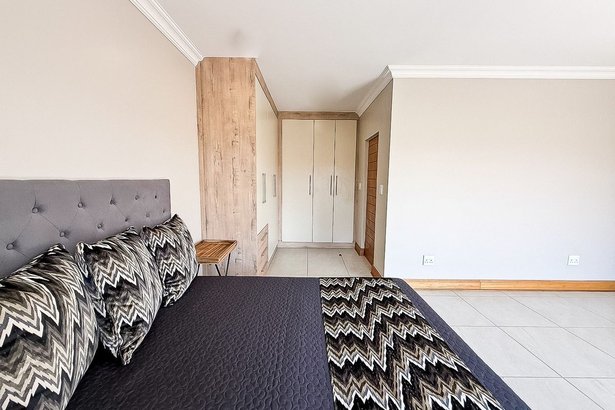 A well-maintained bedroom featuring neutral walls, tiled flooring, and modern built-in cupboards with wood-grain accents.