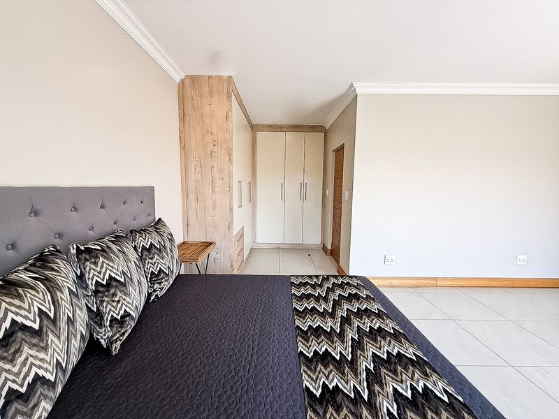 A well-maintained bedroom featuring neutral walls, tiled flooring, and modern built-in cupboards with wood-grain accents.