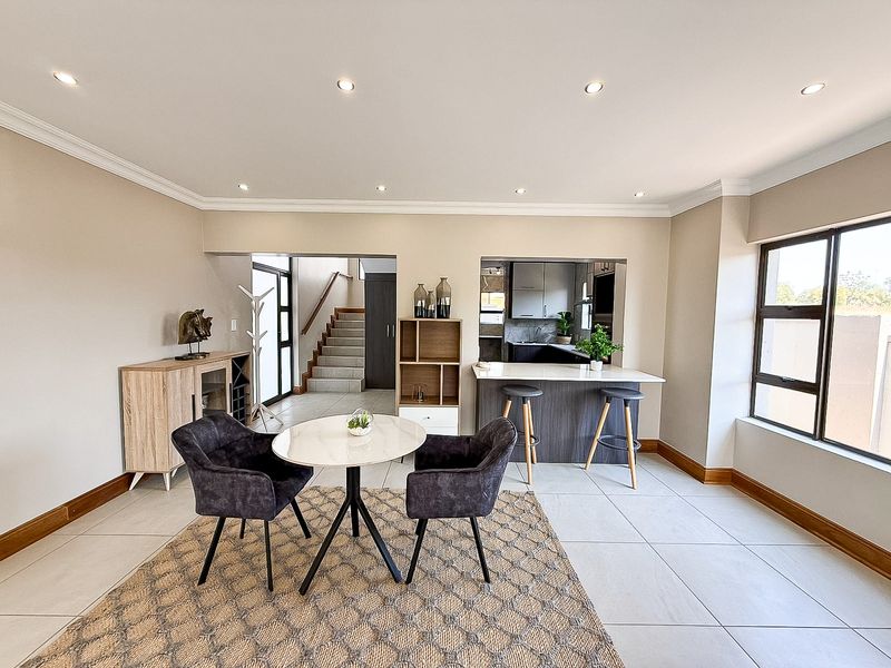 Open-plan living and dining area featuring tiled floors, recessed lighting, and a breakfast bar connecting to the kitchen, with an adjacent staircase.