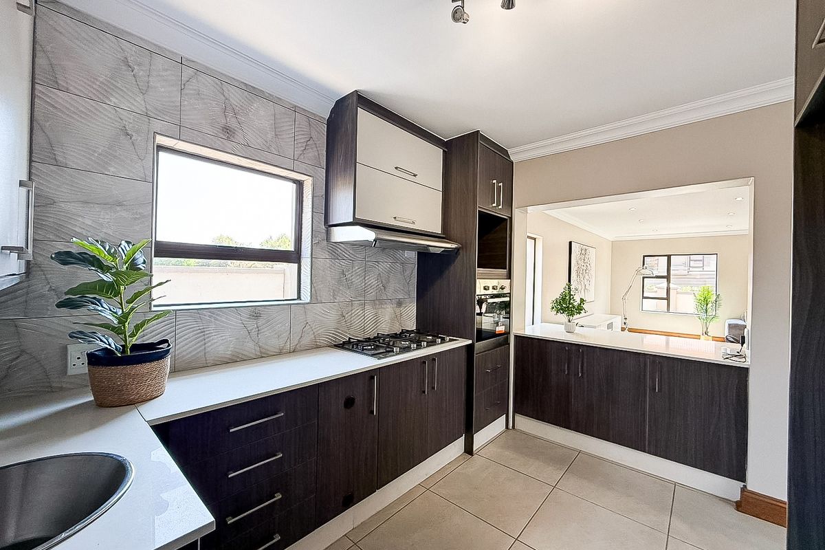 Modern kitchen featuring dark wood cabinetry, stone countertops, gas hob, built-in oven, and a tiled splashback, with an open-plan layout connecting to the living area.