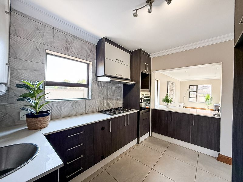 Modern kitchen featuring dark wood cabinetry, stone countertops, gas hob, built-in oven, and a tiled splashback, with an open-plan layout connecting to the living area.