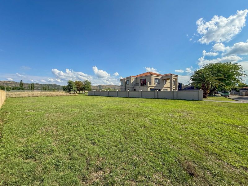 A spacious, level residential plot featuring a well-maintained lawn, enclosed by a perimeter wall, with a neighboring property visible in the background.