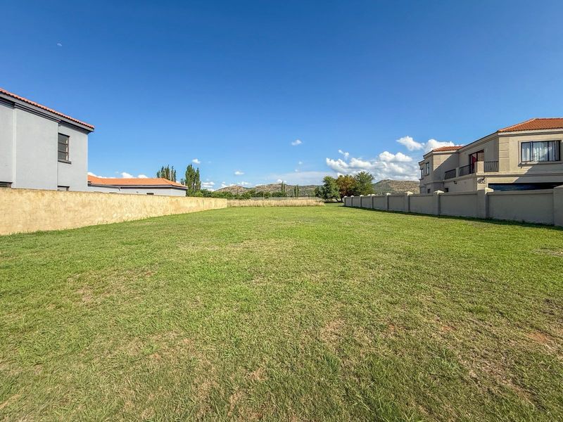 A vacant residential plot featuring a well-maintained grass lawn, enclosed by boundary walls between existing neighboring properties.